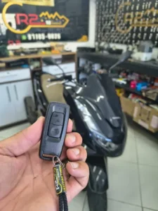 Mão segurando chave de presença Smart Key de moto Honda PCX preta em oficina de chaveiro automotivo na Zona Sul.